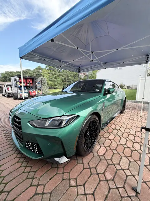 Glossy green coupe beneath a blue canopy with detailing equipment nearby